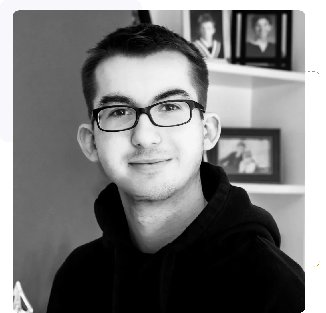Young man with glasses smiling indoors against a blurred background.