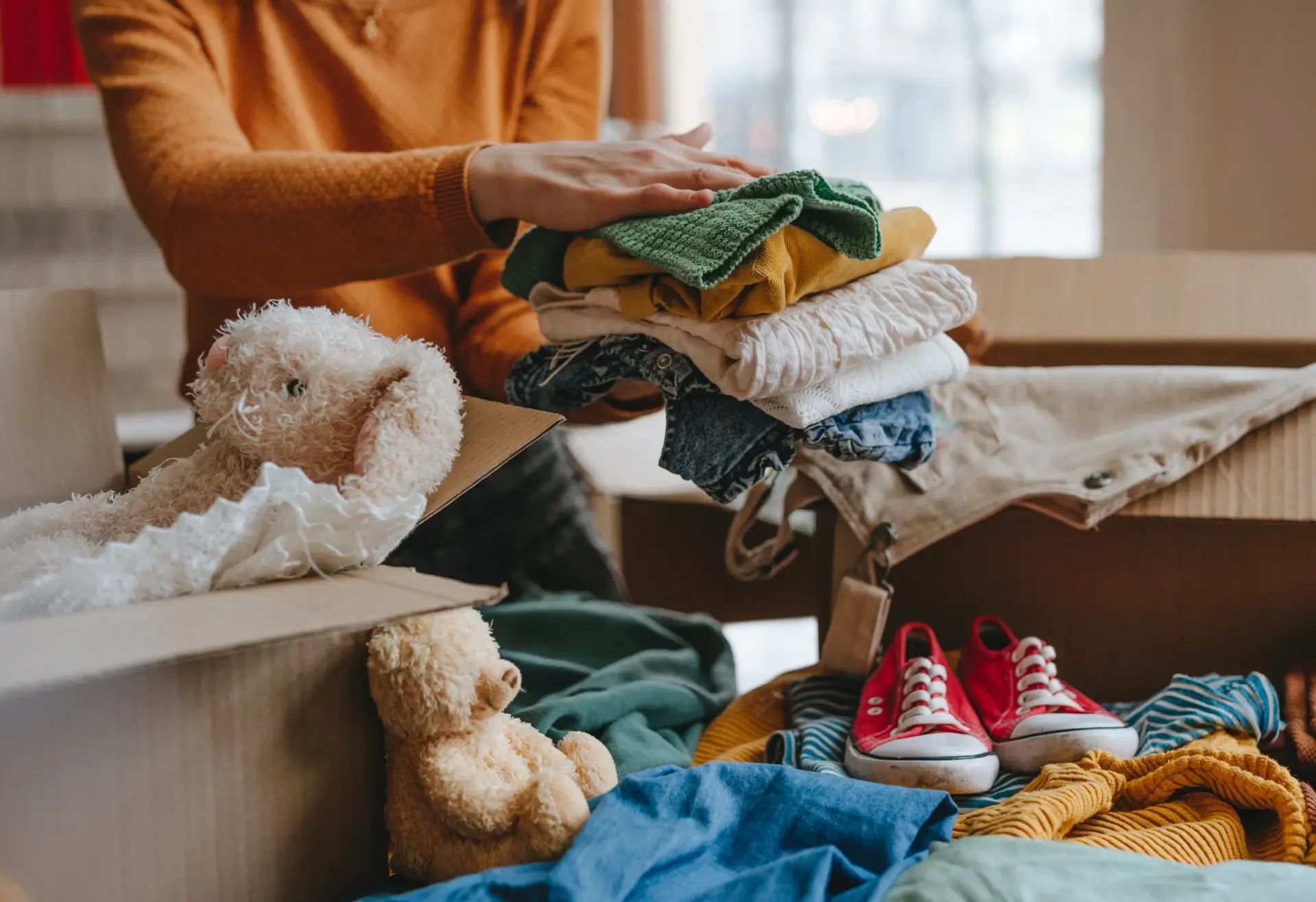 A person folding baby clothes on a bed surrounded by toys.